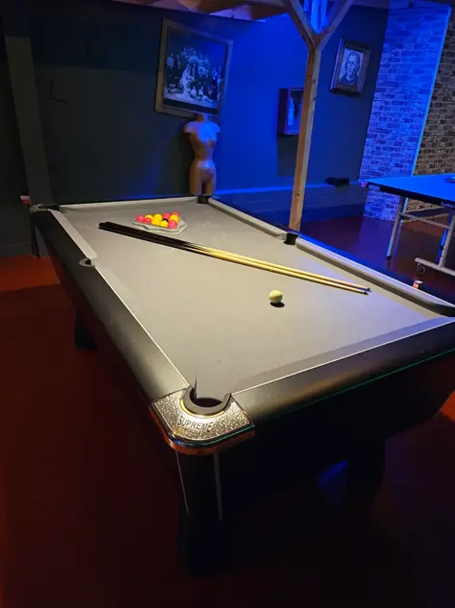 Pool table with cues and balls in a dimly lit room.
