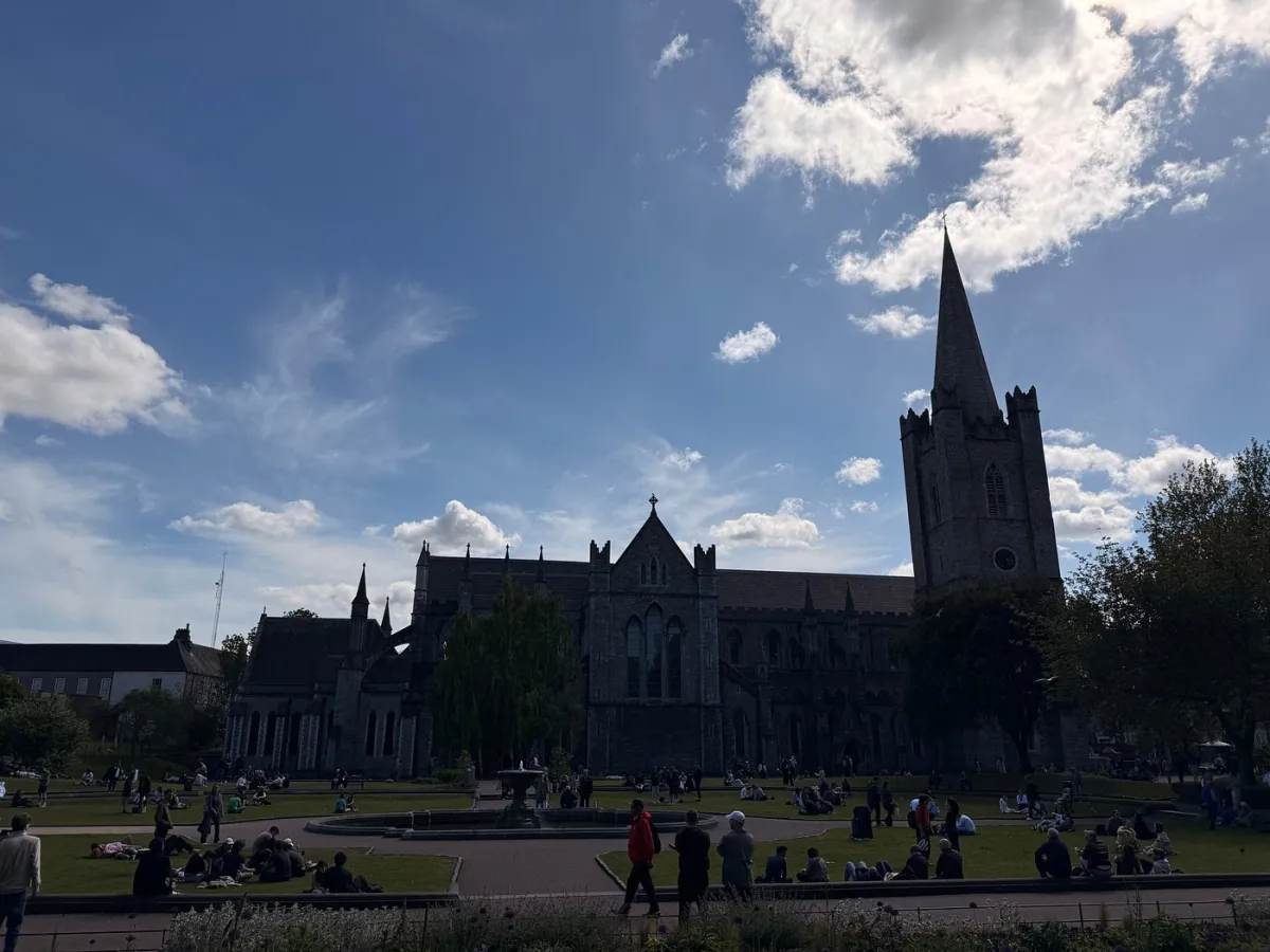 People relaxing in a park near a large cathedral.