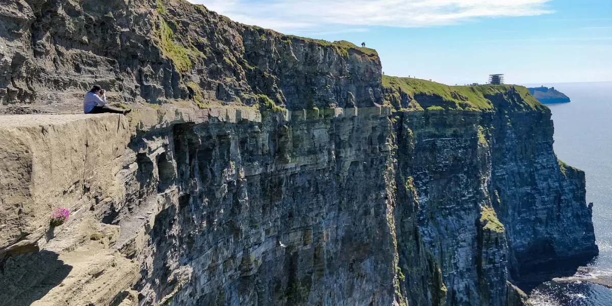 Person sitting on the edge of a cliff overlooking the ocean.