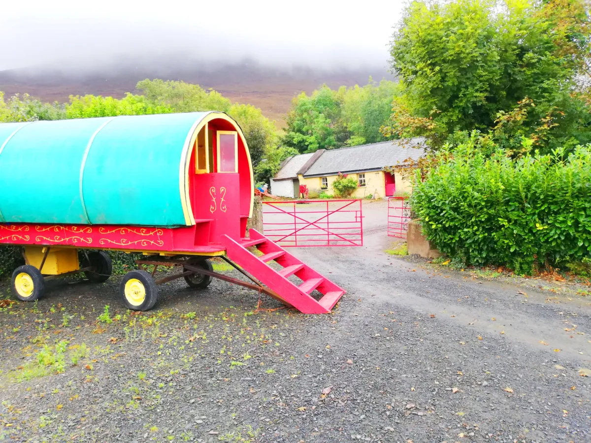 Colorful caravan with steps beside a rural house.