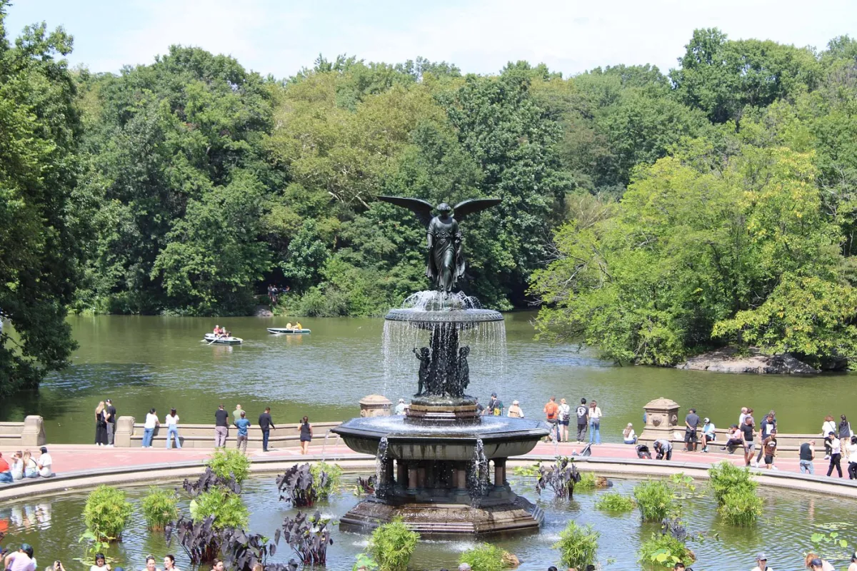 Fountain with angel statue in a park with people around.