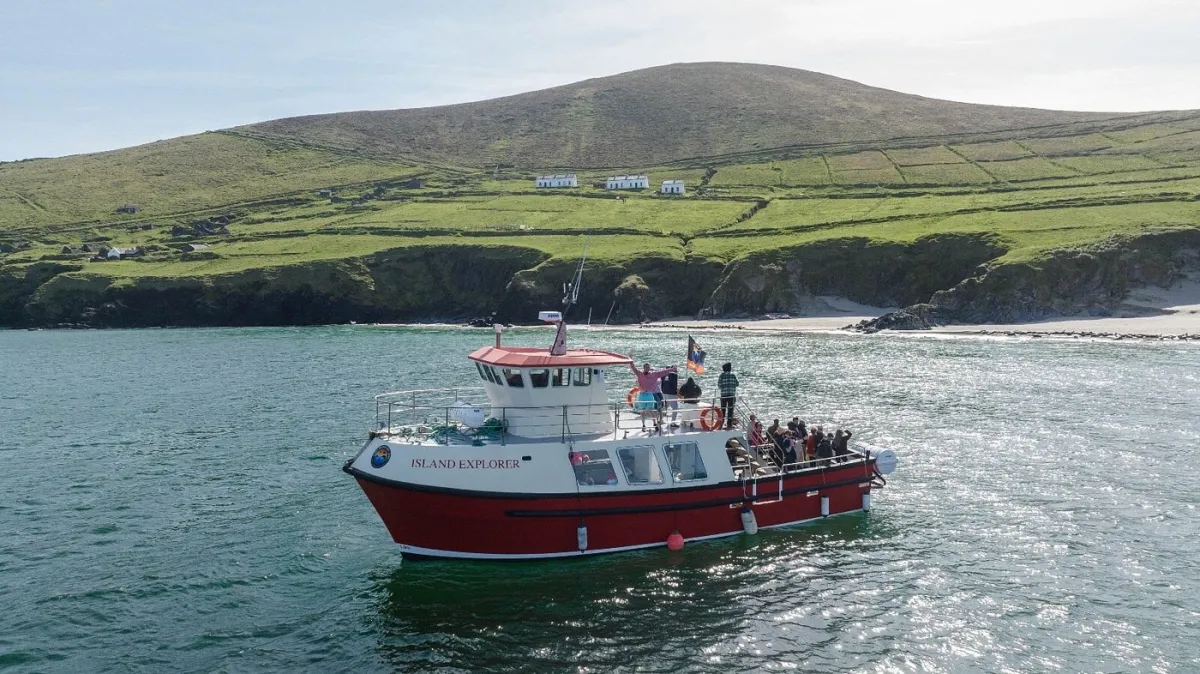 Boat named Island Explorer on water near a green hillside