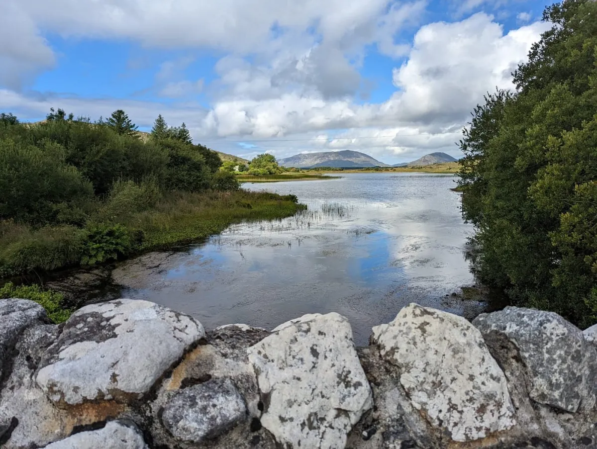 Stone wall overlooking a lake with mountains and trees.