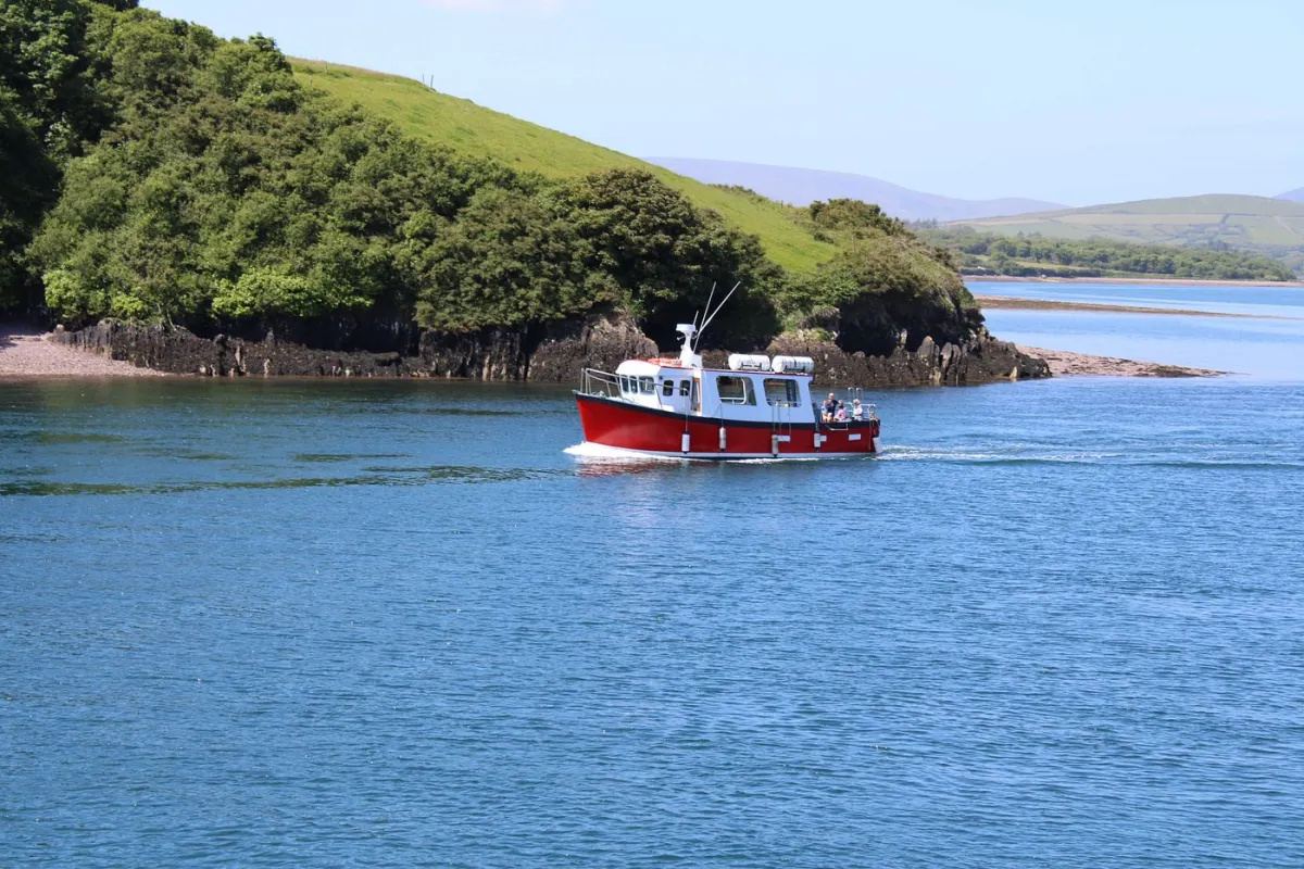Red and white boat on a blue lake near green hills