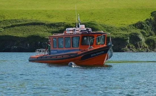 Orange boat on a calm river with green hills in the background.
