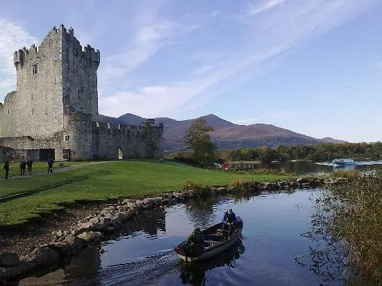 Castle by a lake with a boat and mountains in the background.