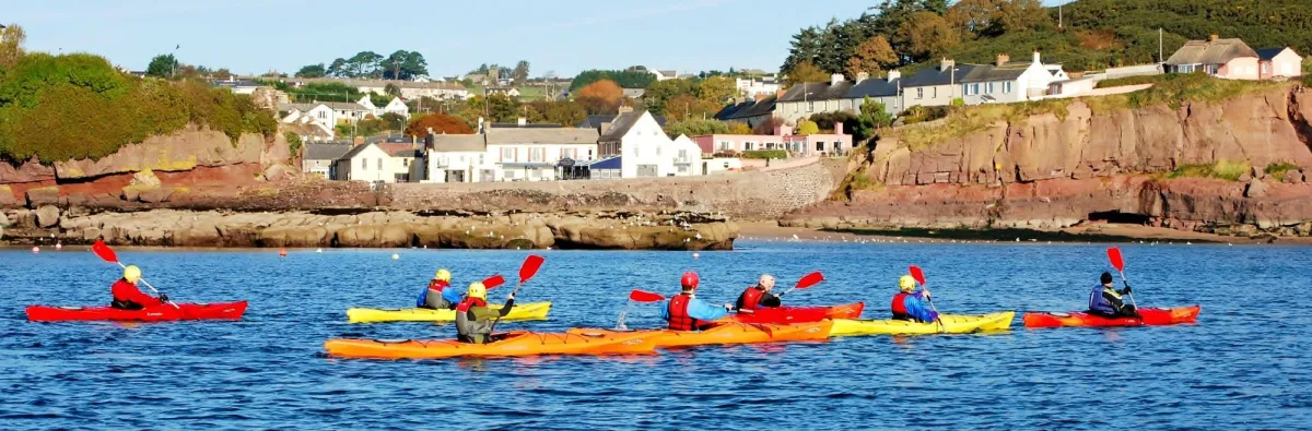 Group of kayakers on a calm sea near a coastal village.