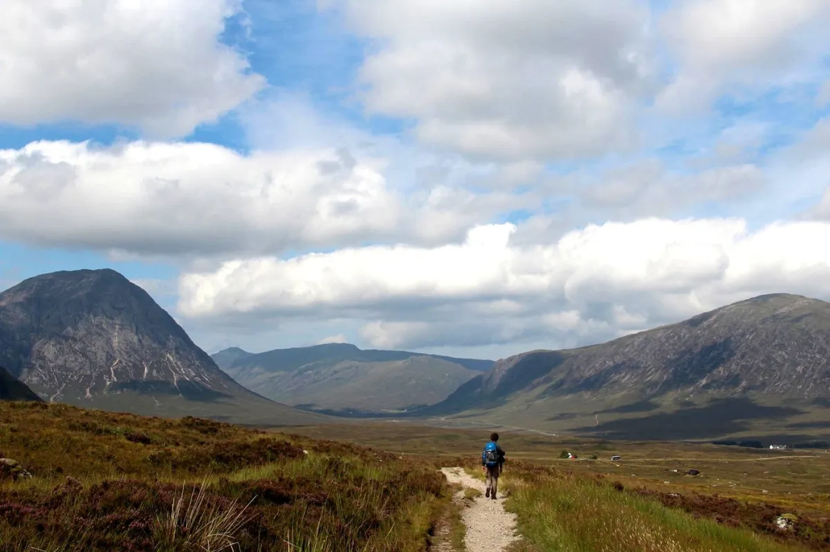 Hiker walking on a trail through a mountain valley.