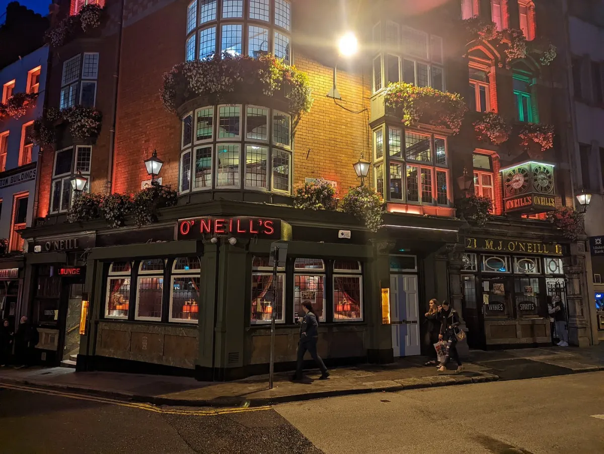 Exterior of O'Neill's pub at night with people walking by.