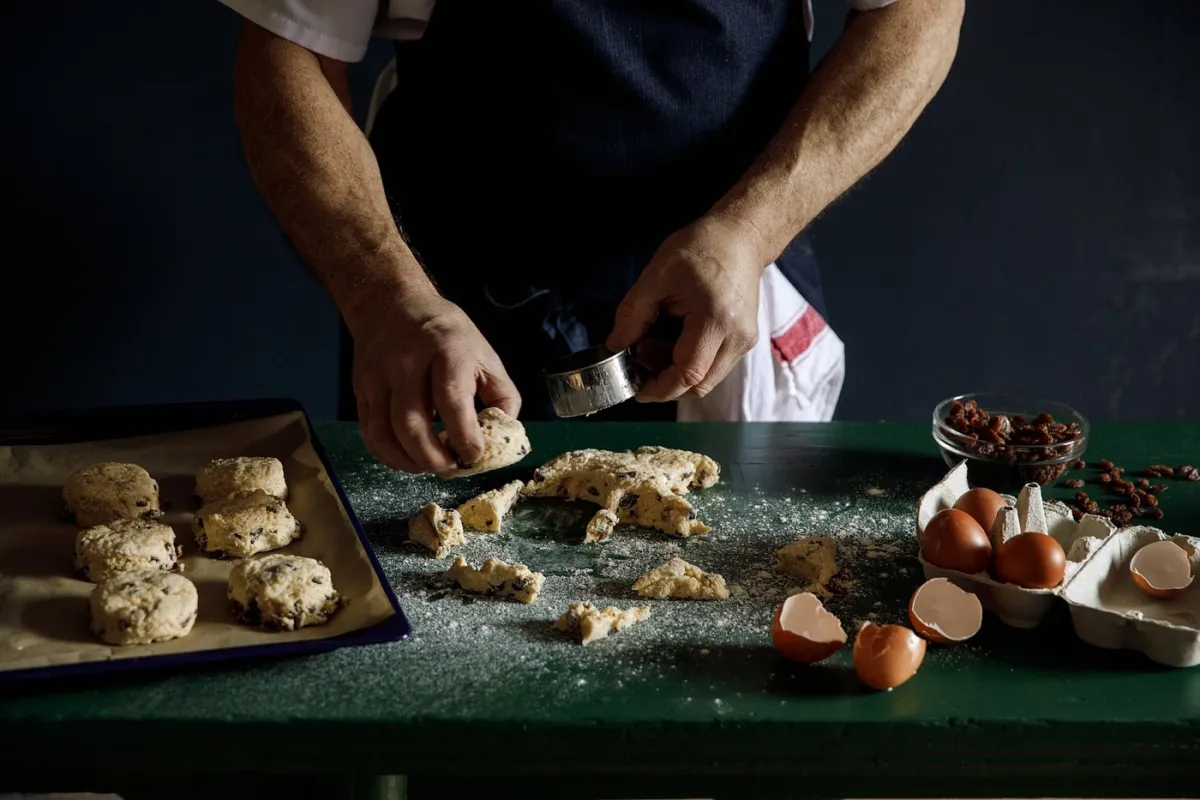 Person preparing scones with dough and ingredients.