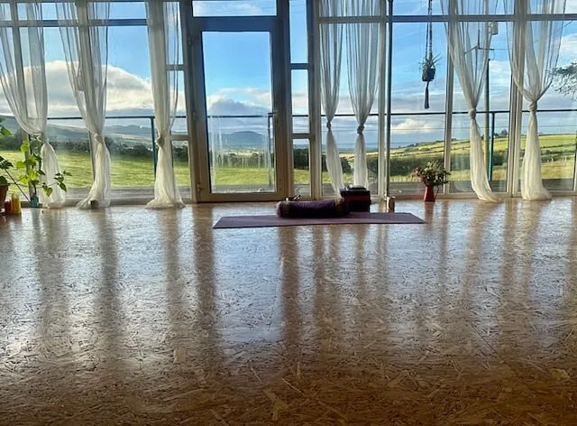 Yoga mat and props in front of large windows with countryside view.