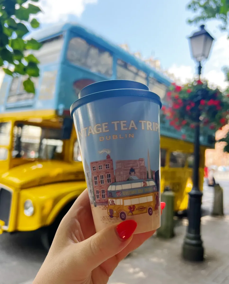 Hand holding a Vintage Tea Trip cup with a bus in background.