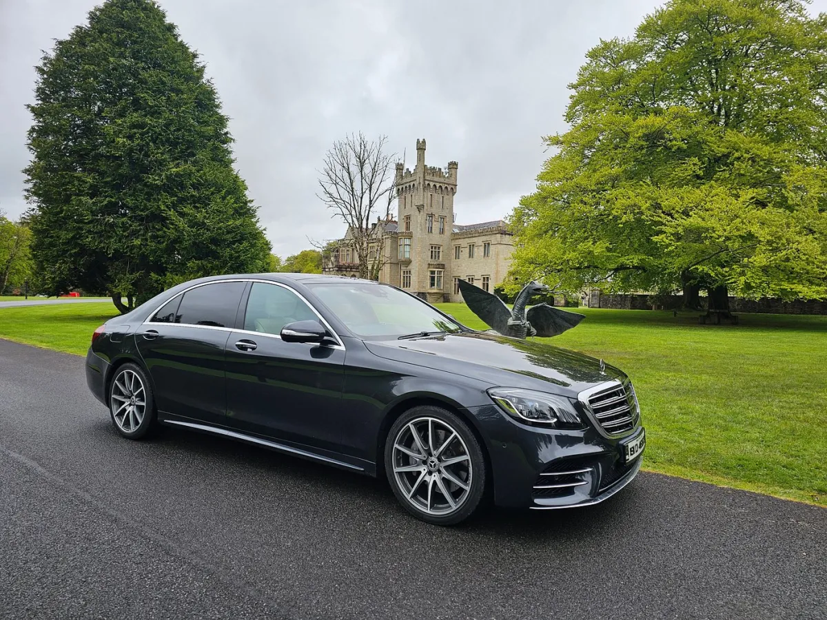 Black car parked in front of a castle with a dragon statue.
