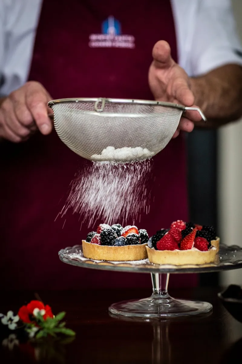 Chef dusting powdered sugar on berry tarts