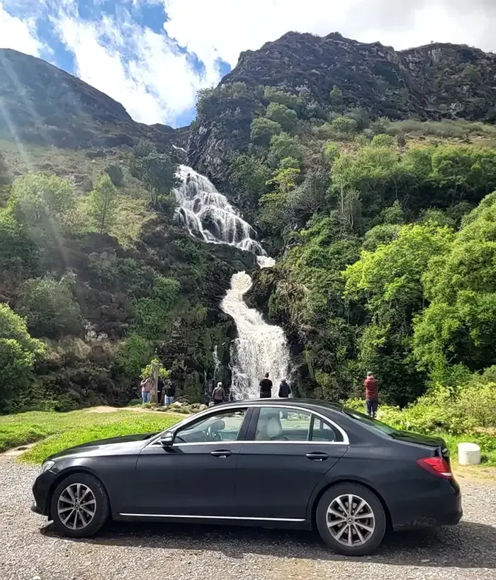 Car parked near a scenic waterfall with mountains.