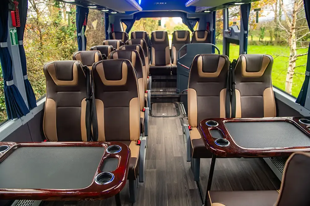 Interior of a luxury minibus with leather seats and tables.