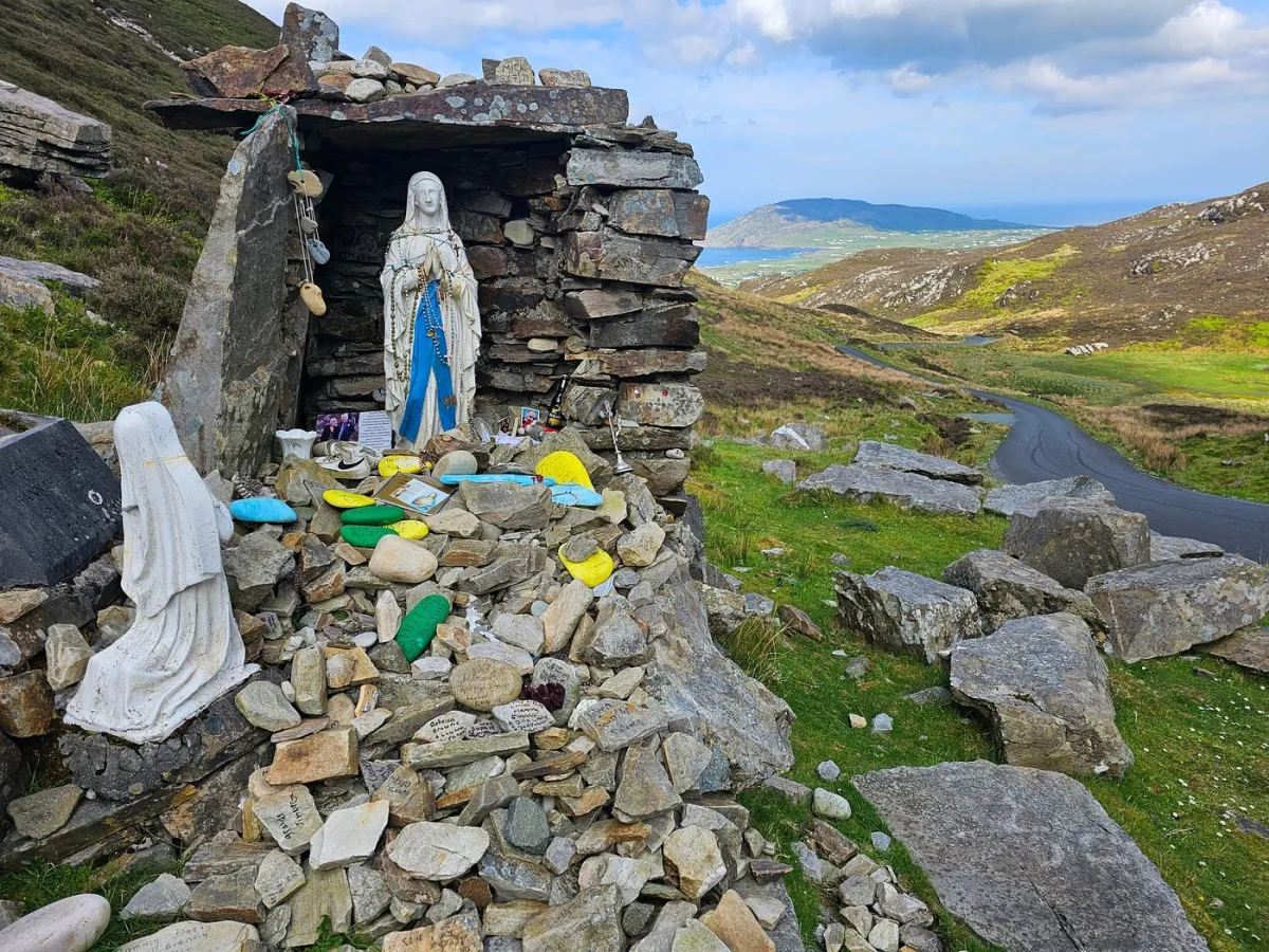 Stone shrine with religious statues and offerings on a hillside.