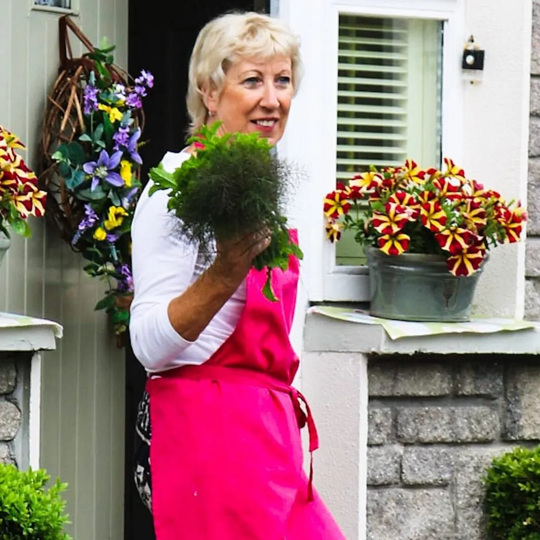 Woman in pink apron holding herbs outside a house