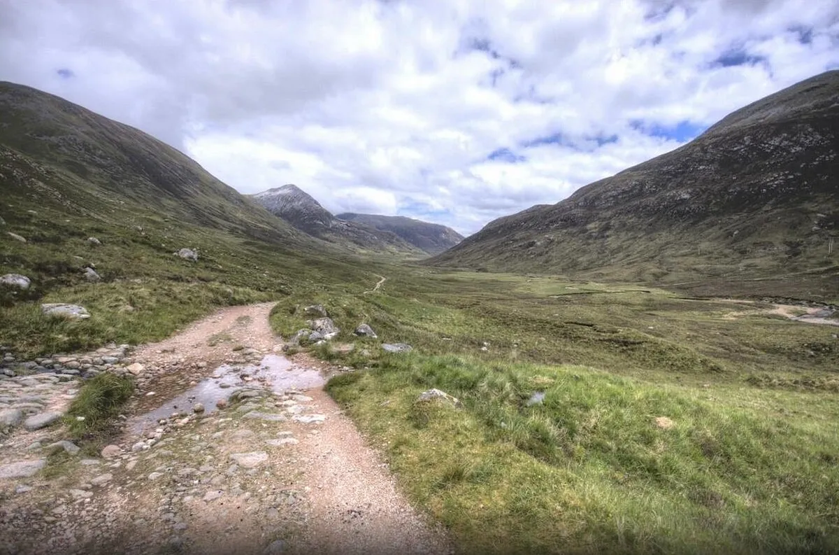 Mountain valley with dirt path and cloudy sky