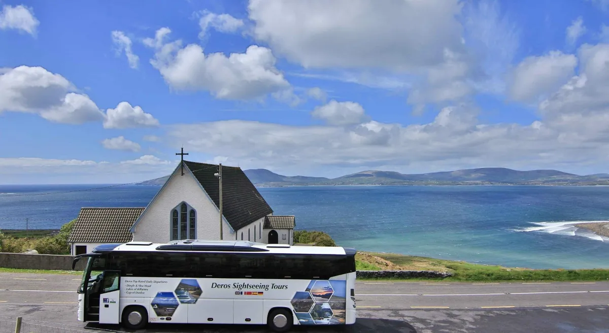 Tour bus near a church overlooking the sea and mountains.
