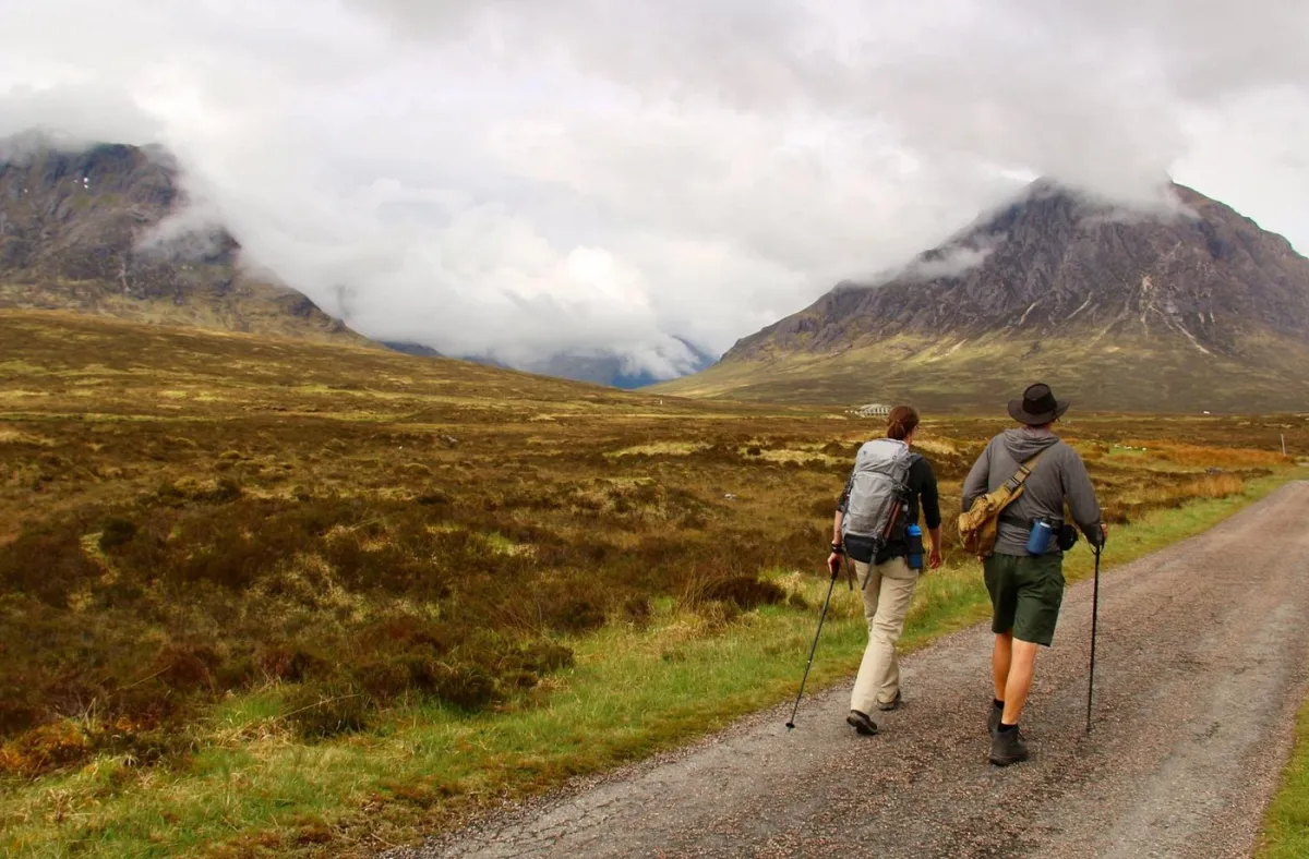Two hikers walking on a path with mountains in the background.