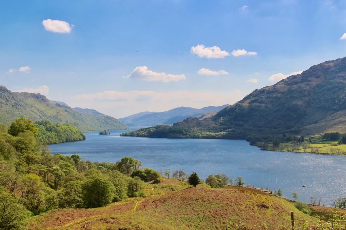 Scenic view of a lake surrounded by hills and greenery.