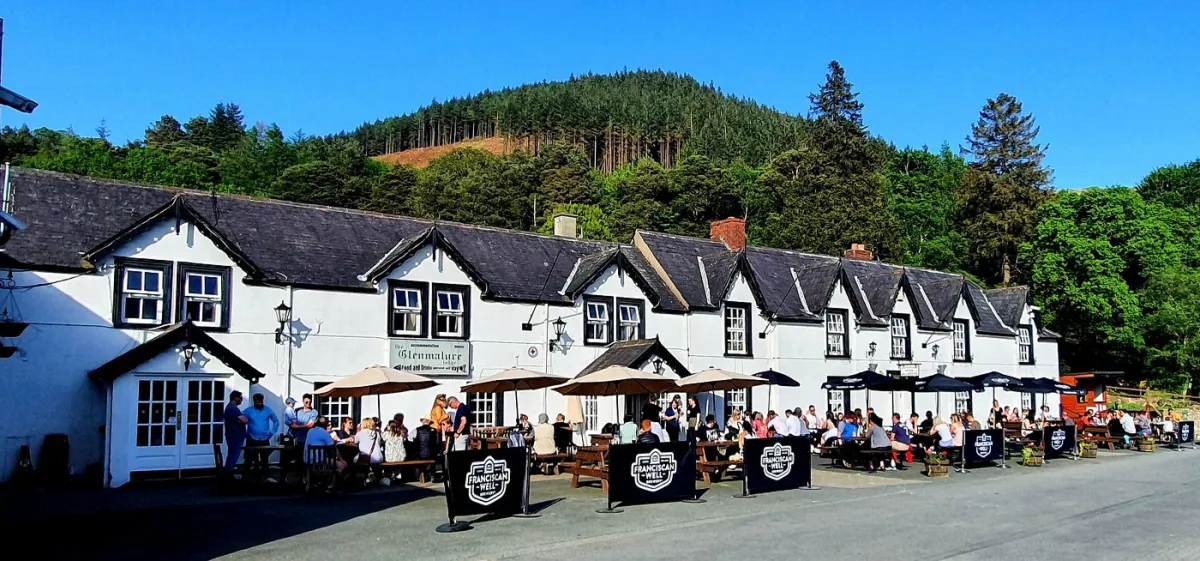 People sitting outside a pub with a forested hill behind.