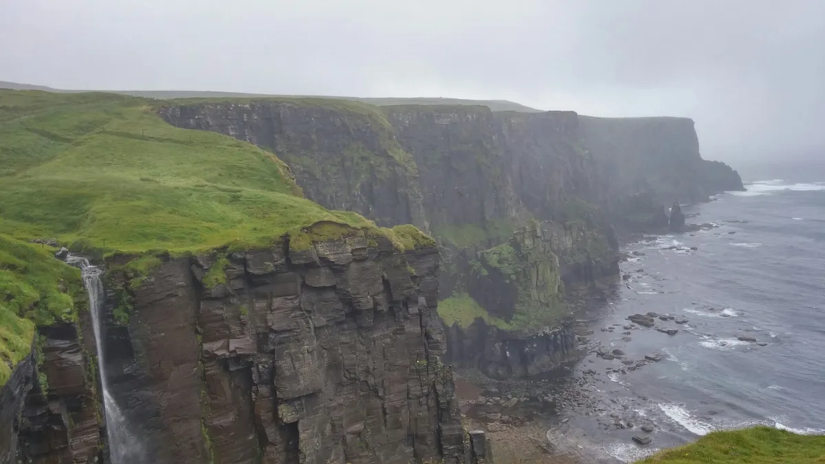 Cliffs with green grass and a waterfall by the sea
