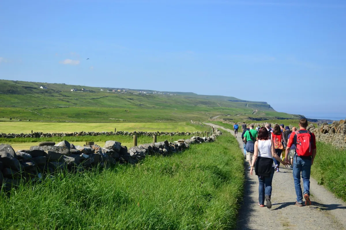 Group of people walking on a rural path with stone walls.