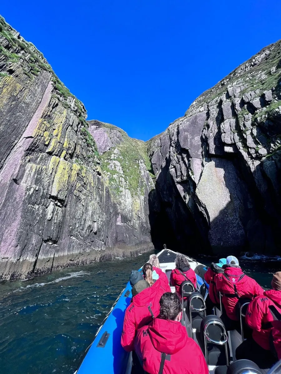 People in a boat approaching a rocky cliff.