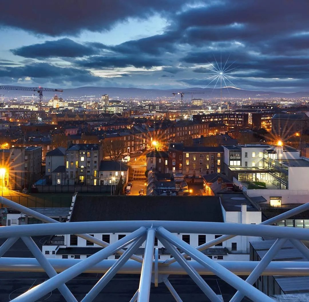 City skyline at dusk with illuminated buildings and cloudy sky.