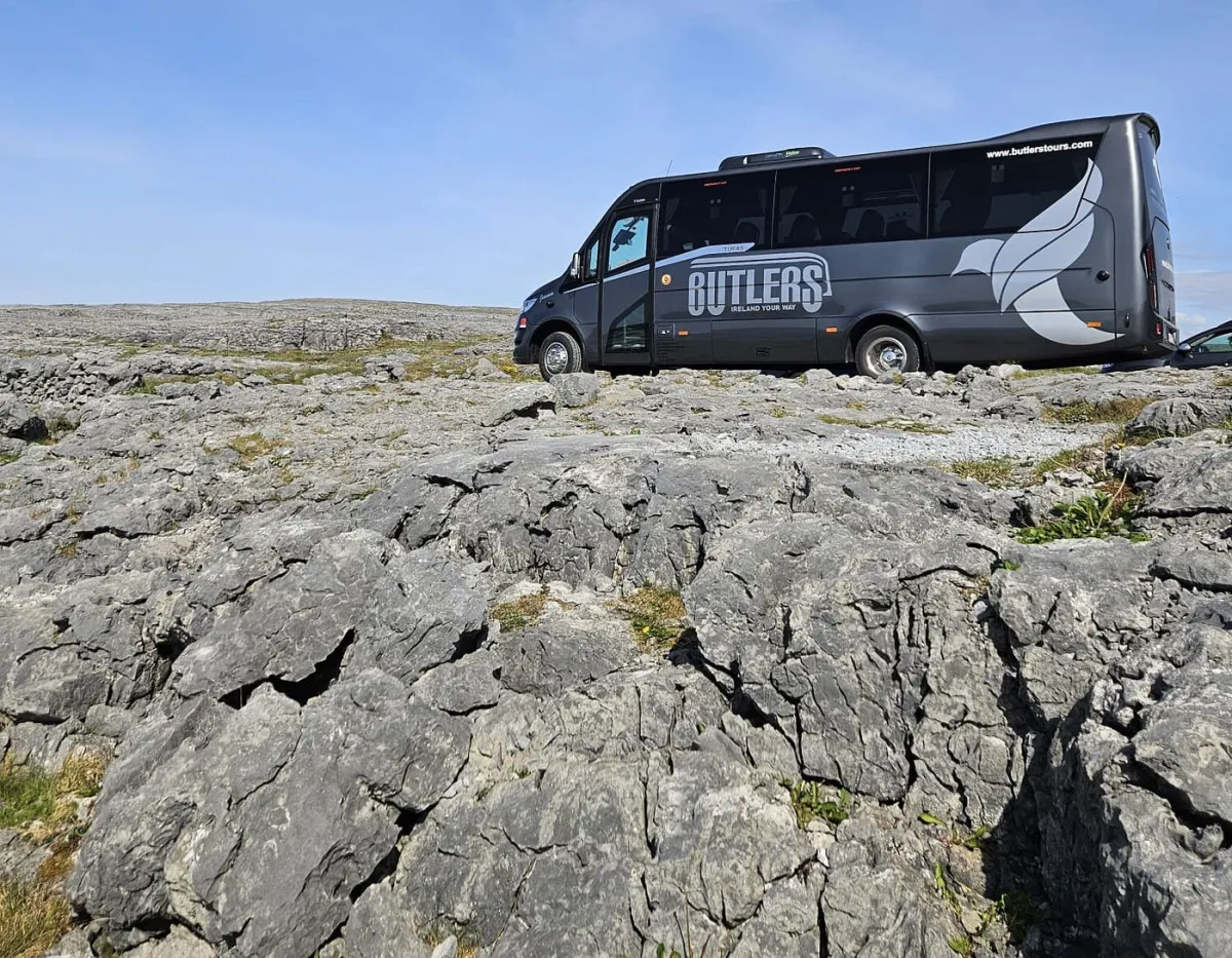 Tour bus parked on rocky terrain under a clear sky.