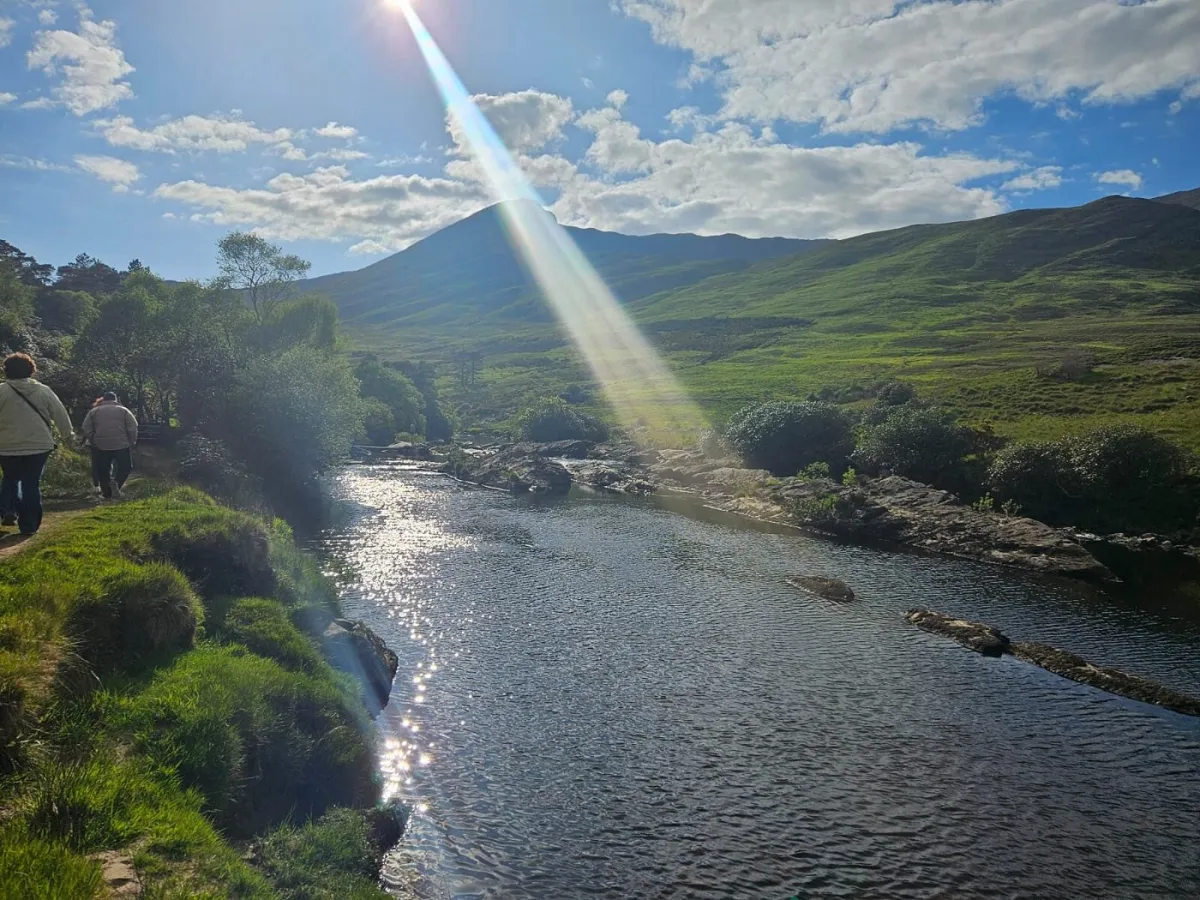 People walking by a river under a sunny sky.