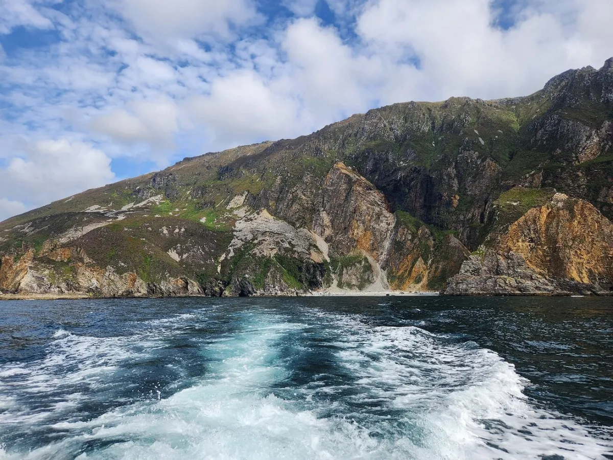 Ocean waves trailing a boat near rocky cliffs.