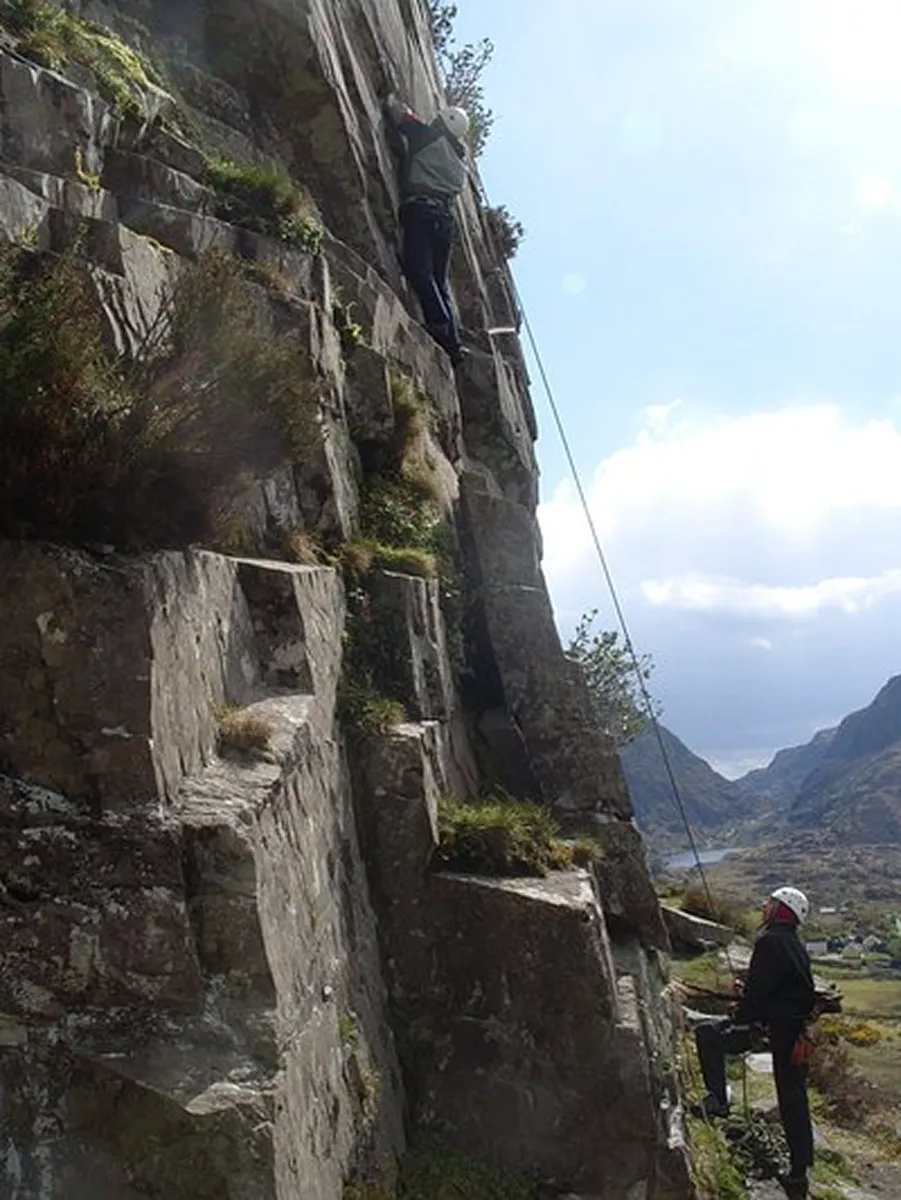 Two people rock climbing on a steep cliff.