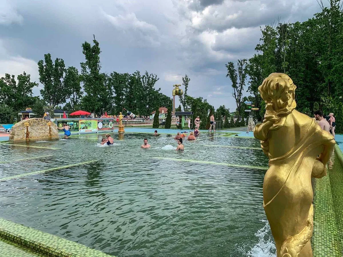 Люди купаються в басейні з золотою статуєю.