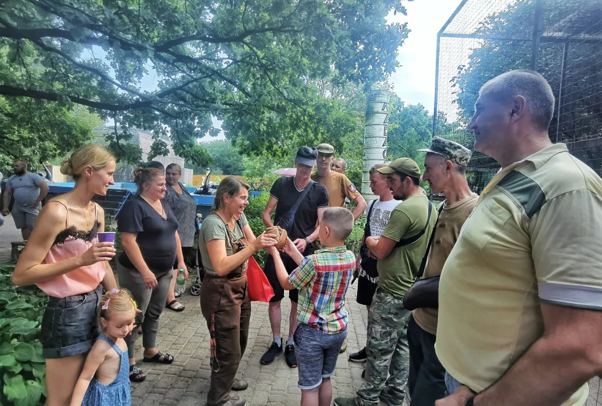 Група людей на відкритому повітрі, жінка передає предмет хлопчику.