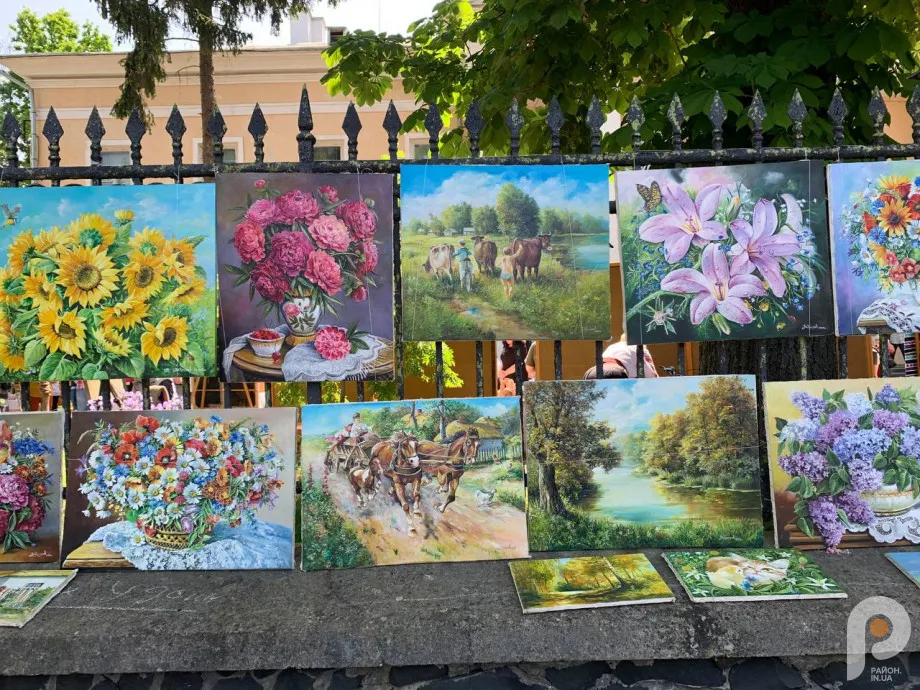 Картини з квітами та пейзажами на вуличній виставці.