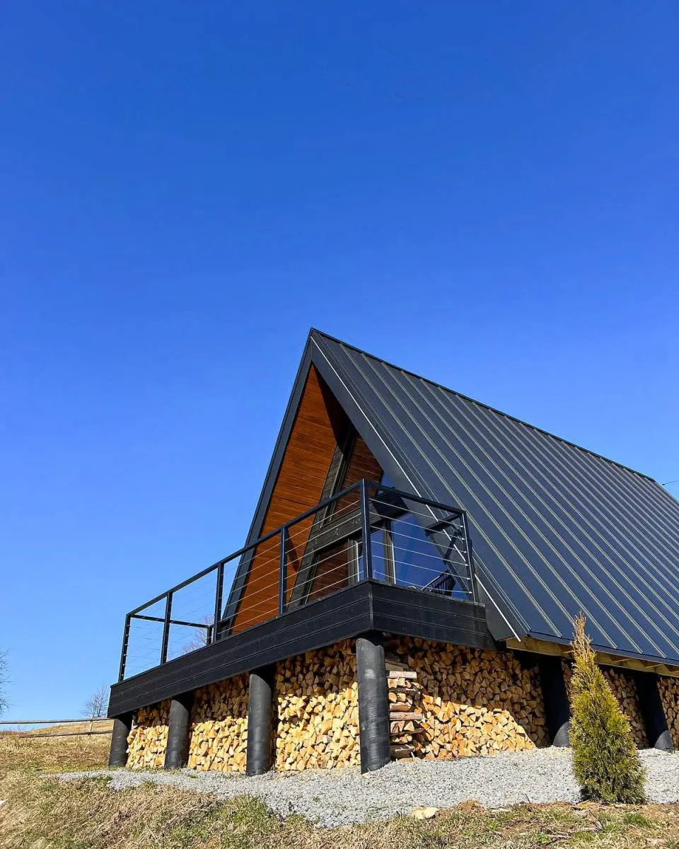 Тераса та дровітня A-frame котеджу на тлі яскраво-синього неба