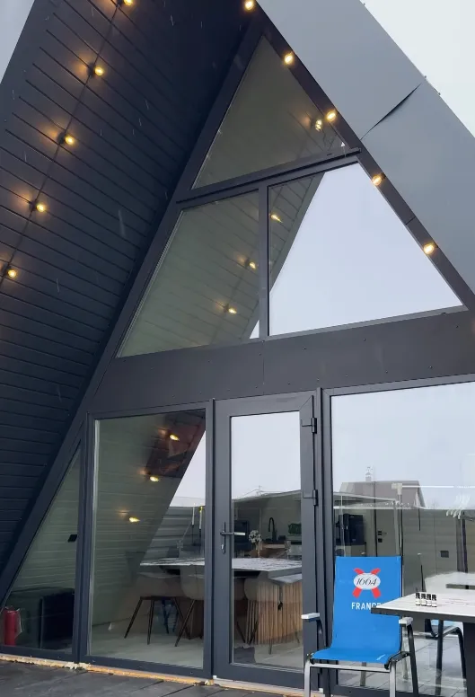 Фасад трикутного котеджу A-Frame з панорамними вікнами та стильними гірляндами у комплексі «Острівок».