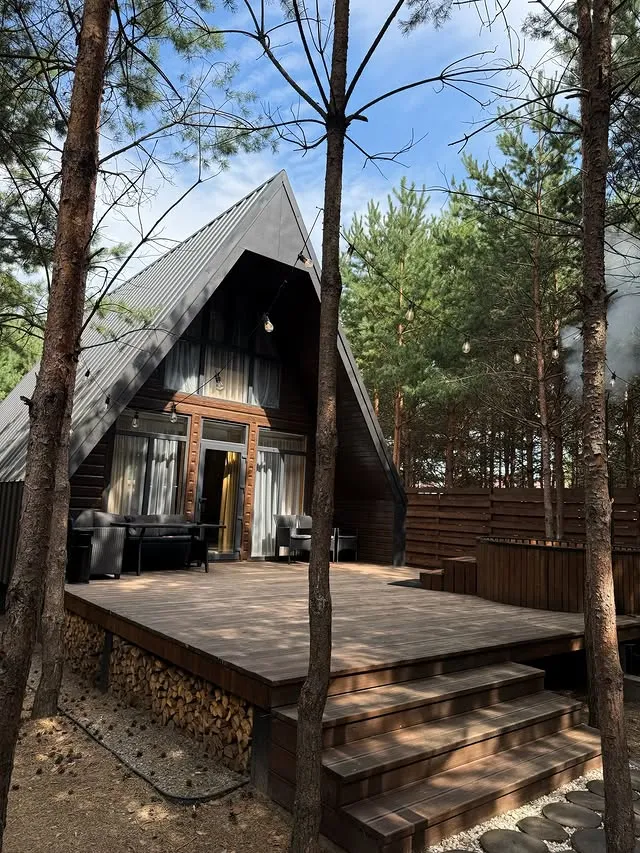 Двоповерховий трикутний котедж A-Frame з просторою терасою, чаном та складеними дровами серед соснового лісу в Grand Forest Лісопіль
