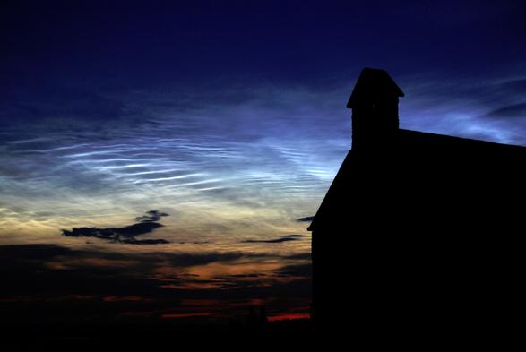 Night time scene, church silhouetted in the foreground against sunlit noctilucent clouds at 82km altitude.