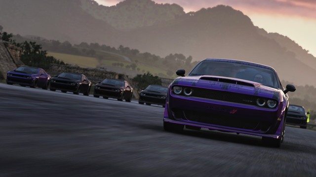 Capture of the front bumper, hood, and windshield of a  black Dodge Challenger SRT Demon with purple two-tone flames from a side angle drag racing on a gravel road with hazy mountains, other cars of the same model, and a sunset in the background.