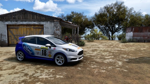 2014 Ford Fiesta ST with a blue and white Ford Livery parked in front of an old brick and wood barn.