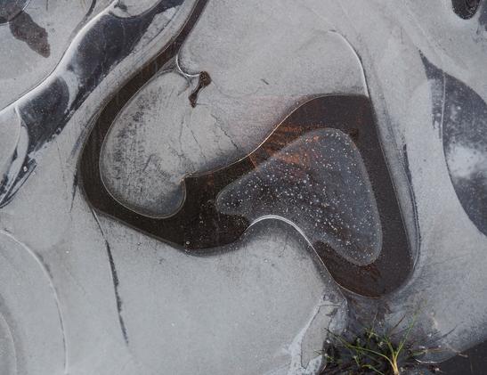 More patterns in a frozen puddle. A dark, golden streak shows through from the depths.
