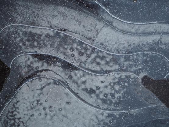 More patterns in a frozen puddle. Looks like overlapping, curving metal plates.