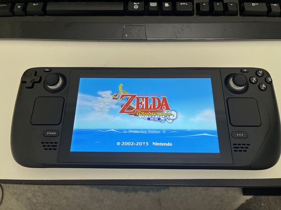 The title screen of “The Legend of Zelda: The WindWaker” being displayed on a Steam Deck, sitting on a desk next to a Keyboard.