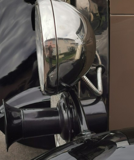 Side view of old fashioned headlamp on a car. The horn and front fender are visible below the light.