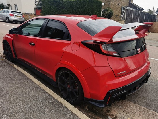 Rear 3/4 view of a red Honda Civic Type R with black alloy wheels. It has a large great spoiler.