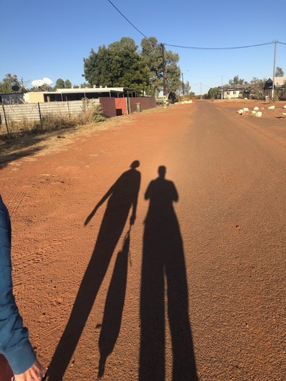Elongated shadows of two people on a red dusty road in a desert community